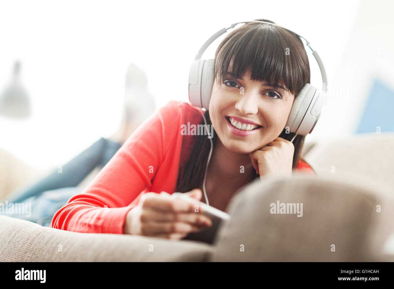 Lächelnde junge Frau zu Hause auf der Couch entspannen, trägt Kopfhörer, sie mit einer digital-Tablette und beobachten ein Streaming-vi Stockfoto