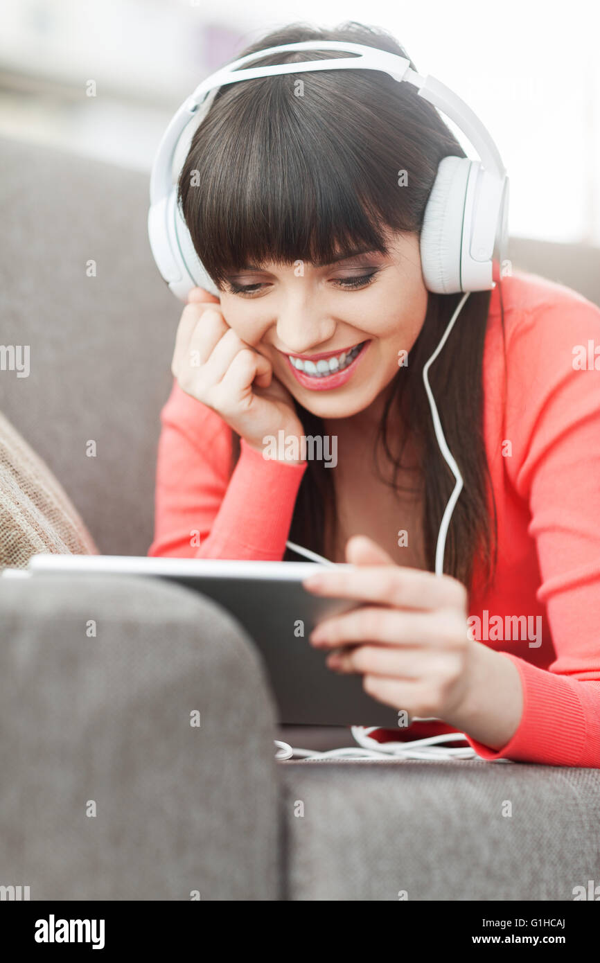 Lächelnde junge Frau zu Hause auf der Couch entspannen, trägt Kopfhörer, sie mit einem digital-Tablette und einen Film online Stockfoto