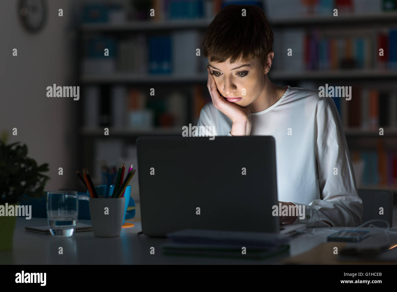 Junge attraktive Frau am Schreibtisch sitzen und arbeiten mit einem Laptop spät in die Nacht Stockfoto