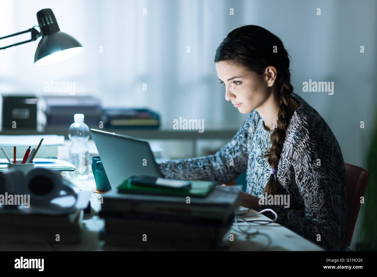 Hübsche junge Studentin sitzt am Schreibtisch und ihre Hausaufgaben, verbindet sie mit dem Internet mit einem Laptop Stockfoto