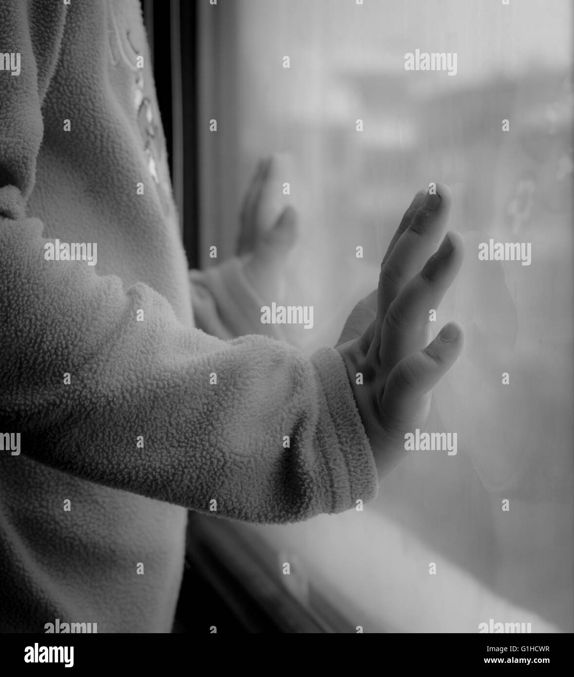 Kind auf der Suche durch das Fenster mit Händen auf das Glas gelegt Stockfoto