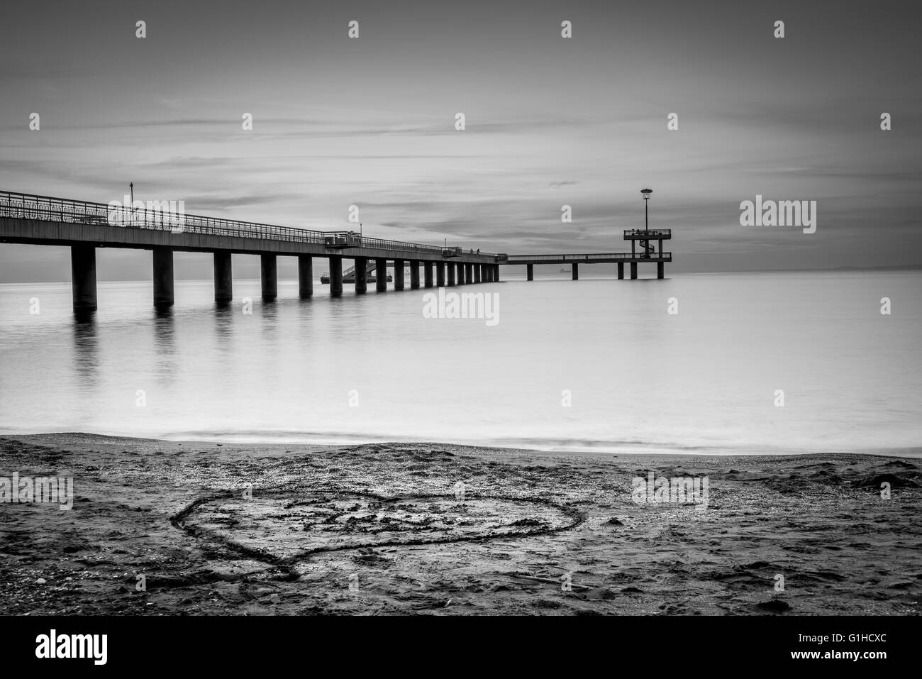 Sonnenaufgang über eine Seebrücke. Herzen in den Sand gezeichnet. Stockfoto