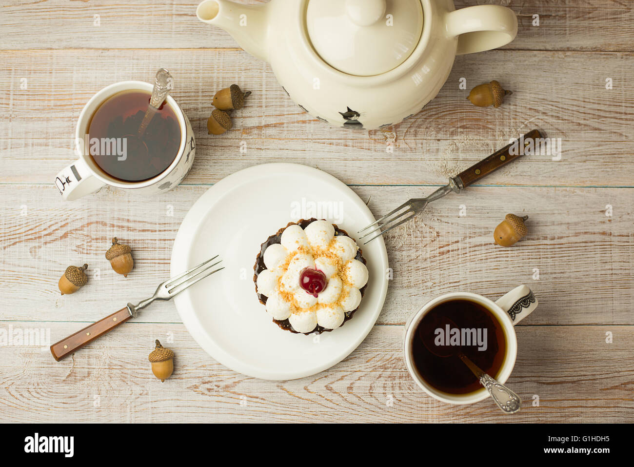 Zwei Tassen Tee und Kuchen mit einer Kirsche auf dem Tisch Stockfoto