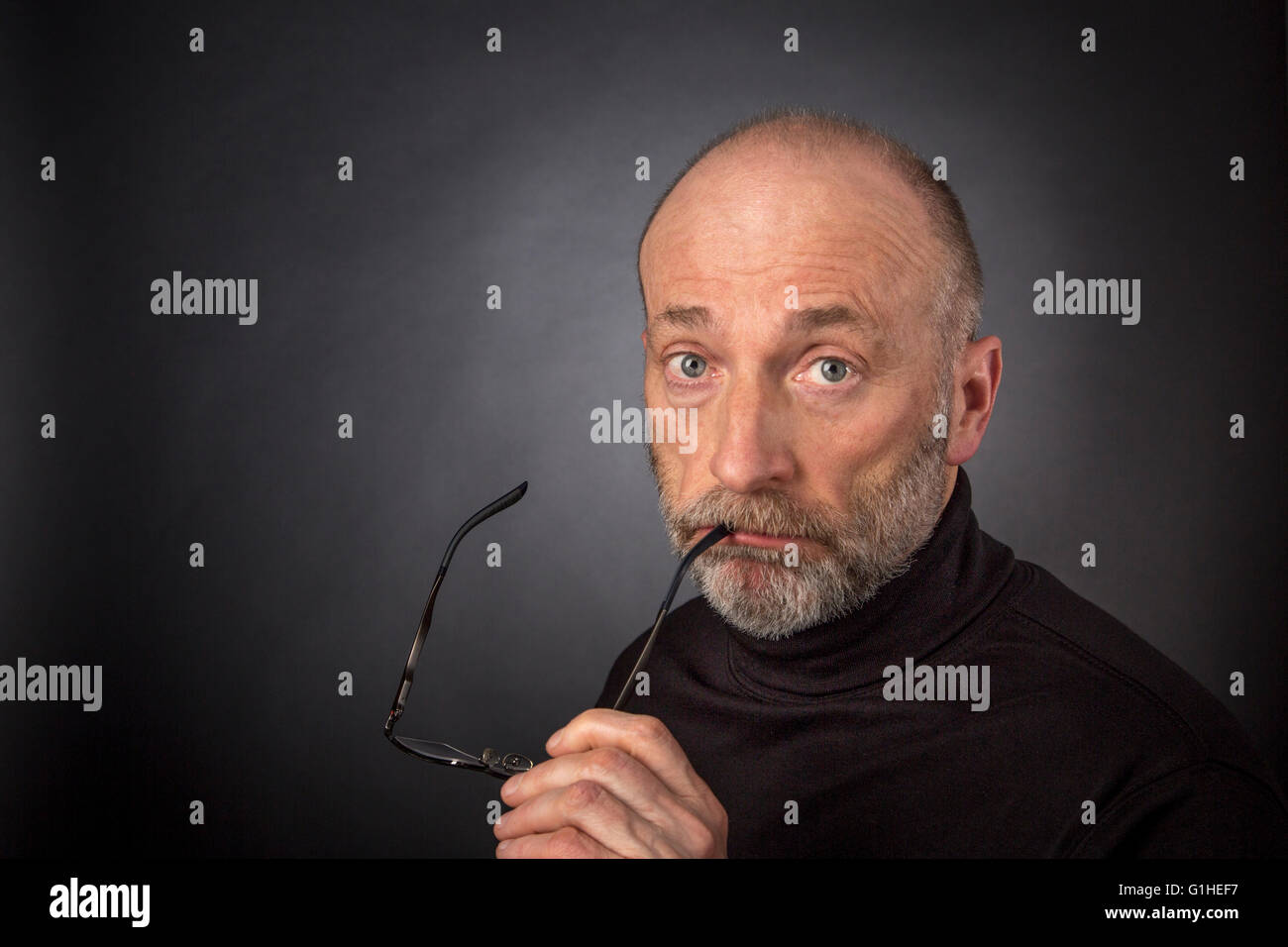 60 Jahre alter Mann mit Bart und lesen Gläser - ein Kopfschuss vor einem schwarzen Hintergrund Stockfoto