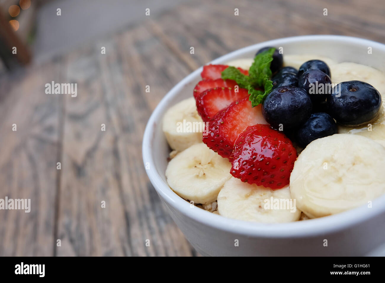 Acai Schüssel mit frischem Obst, Erdbeere, Heidelbeere, Banane und Pfefferminze Blätter an der Spitze auf dem Holztisch. Stockfoto