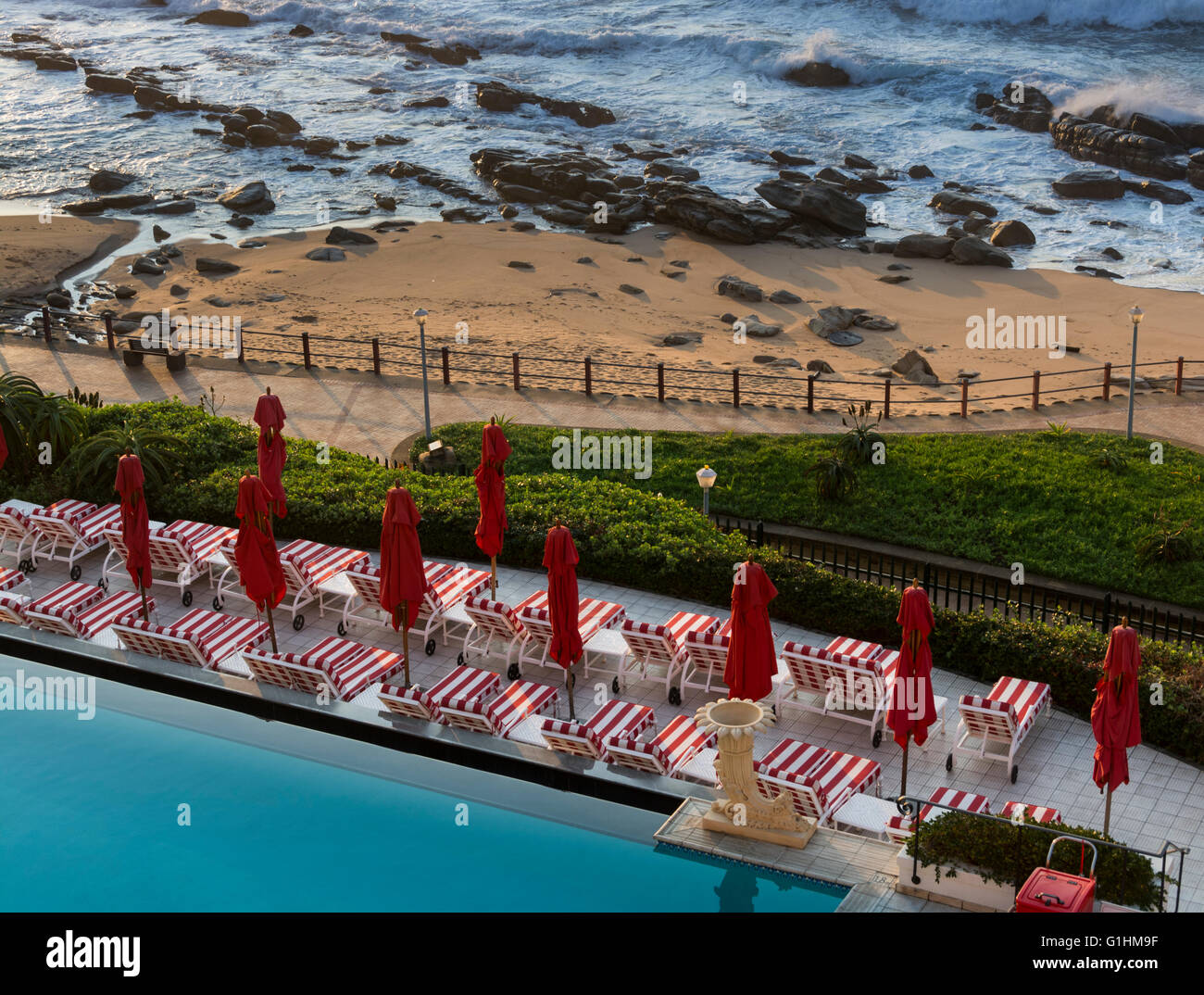 Sonnenliegen und rote Sonnenschirme warten auf Gäste am Pool von einem Luxus-Strandhotel in Durban, KwaZulu Natal, Südafrika Stockfoto