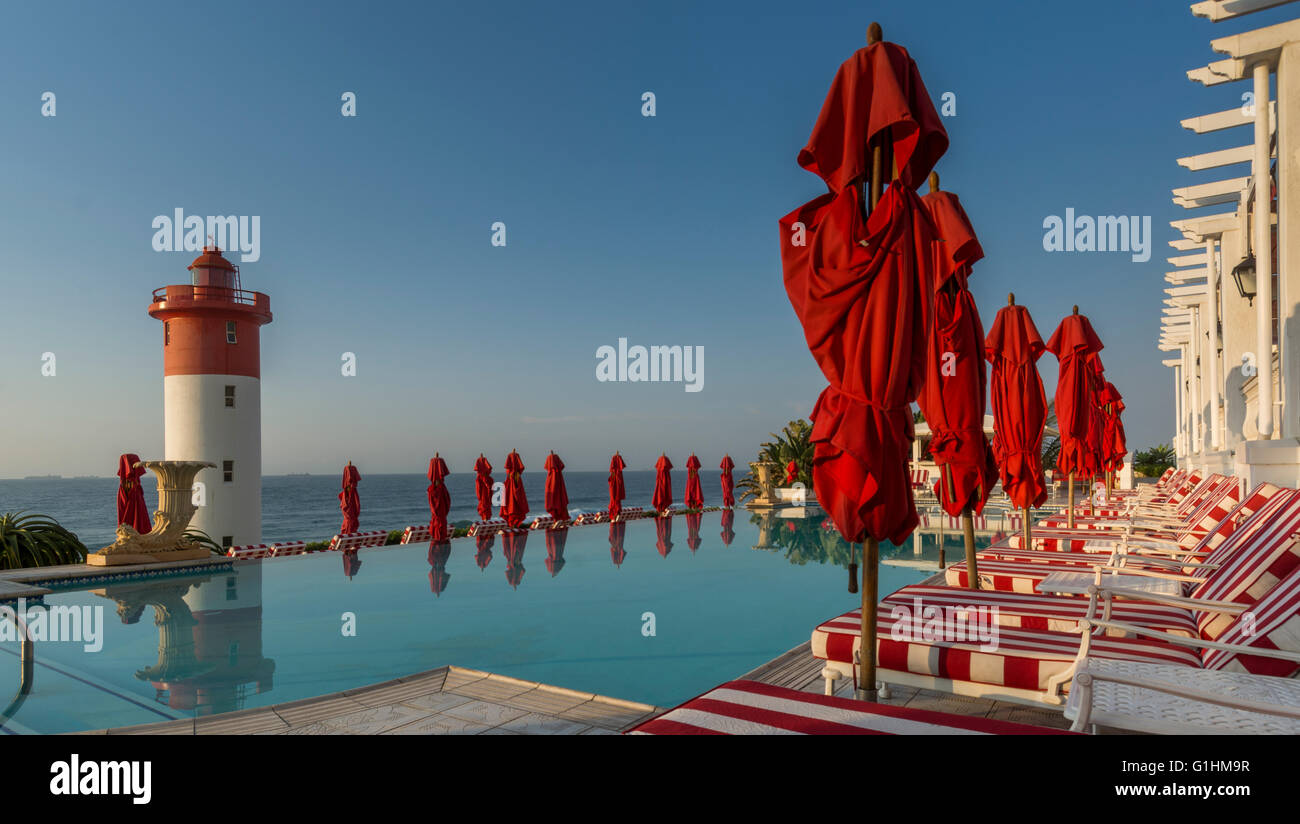 Sonnenliegen und rote Sonnenschirme warten auf Gäste am Pool eines Luxus-Hotels in Durban, KwaZulu Natal, Südafrika Stockfoto