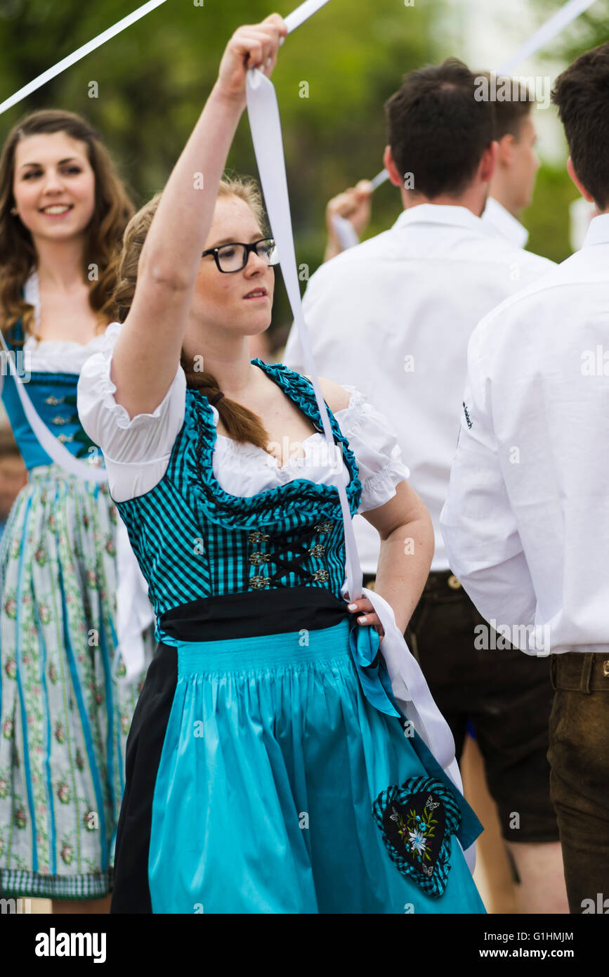Porträt einer jungen Frau in einem Kleid tanzen einen traditionellen bayerischen Volkstanz um einen Maibaum hält ein weißes Band Stockfoto