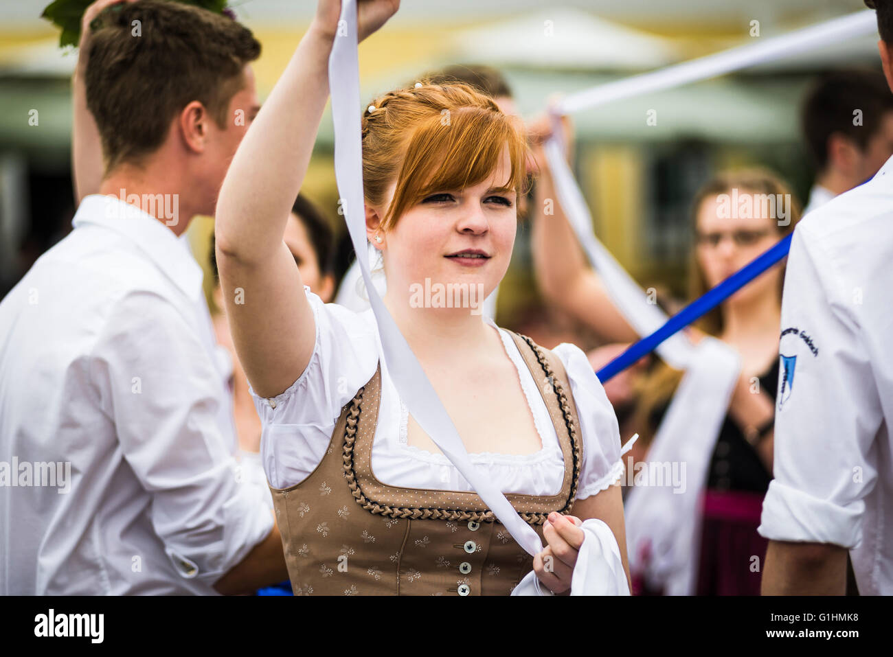 Porträt einer lächelnden jungen Frau in einem Kleid tanzen einen traditionellen bayerischen Volkstanz um einen Maibaum hält ein weißes Band Stockfoto