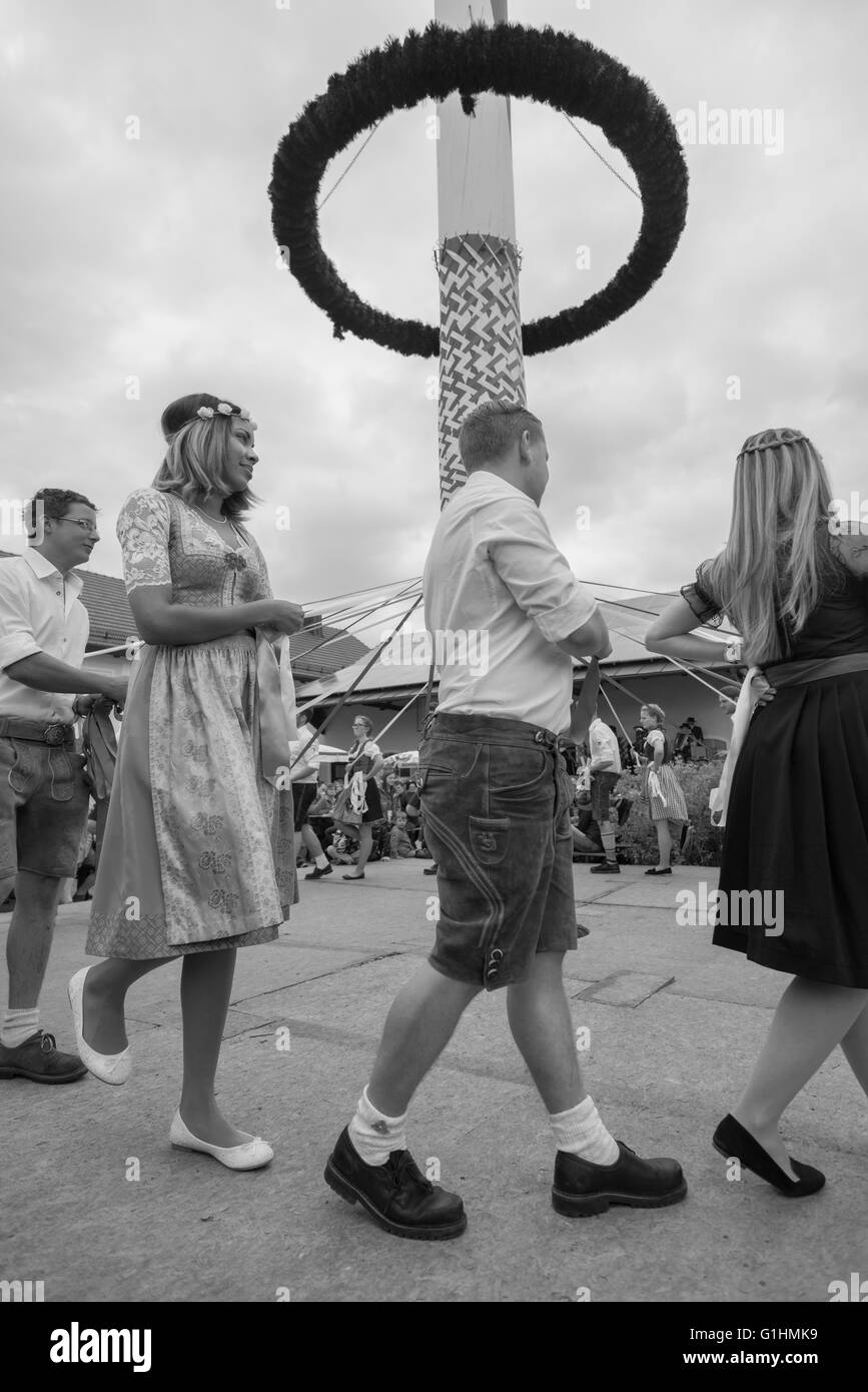 Frauen und Männer in lokalen Kostümen tanzen einen traditionellen bayerischen Volkstanz rund um den Maibaum mit Bändern Stockfoto