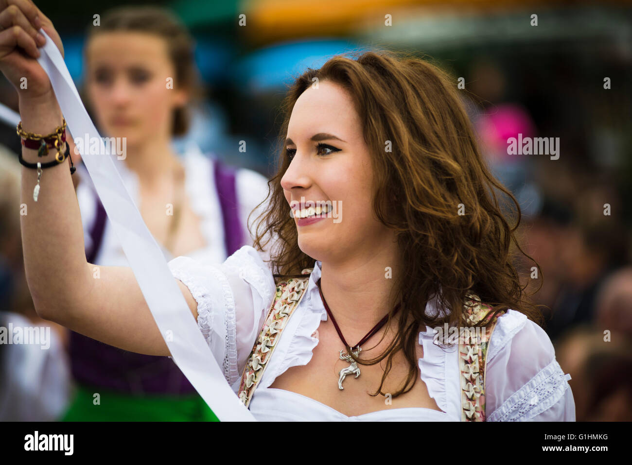 Porträt einer lächelnden jungen Frau in einem Kleid tanzen einen traditionellen bayerischen Volkstanz um einen Maibaum hält ein weißes Band Stockfoto