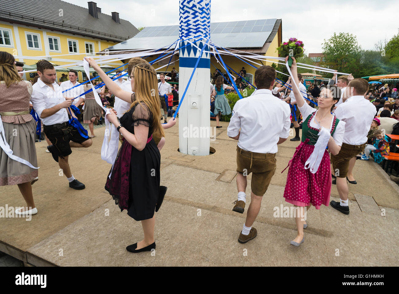 Frauen und Männer in Trachten tanzen eine traditionelle bayerische Volksmusik Tanz um den Maibaum, blaue und weiße Bänder Stockfoto