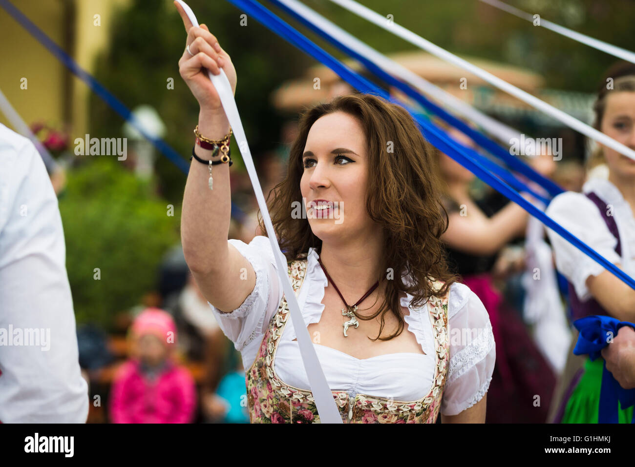 Porträt einer lächelnden jungen Frau in einem Kleid tanzen einen traditionellen bayerischen Volkstanz um einen Maibaum hält ein weißes Band Stockfoto