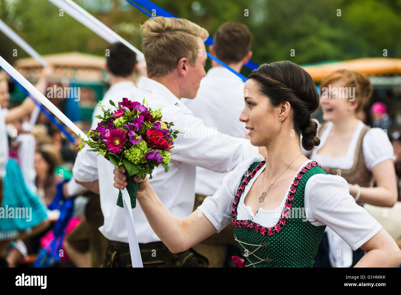 Porträt einer jungen Frau mit Blumenstrauß Tanz einen traditionellen bayerischen Volkstanz um einen Maibaum hält eine Band Stockfoto