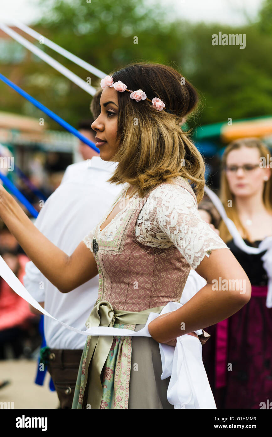Porträt einer dunkelhäutigen jungen Frau in einem Kleid tanzen einen traditionellen bayerischen Volkstanz um einen Maibaum hält eine Band Stockfoto