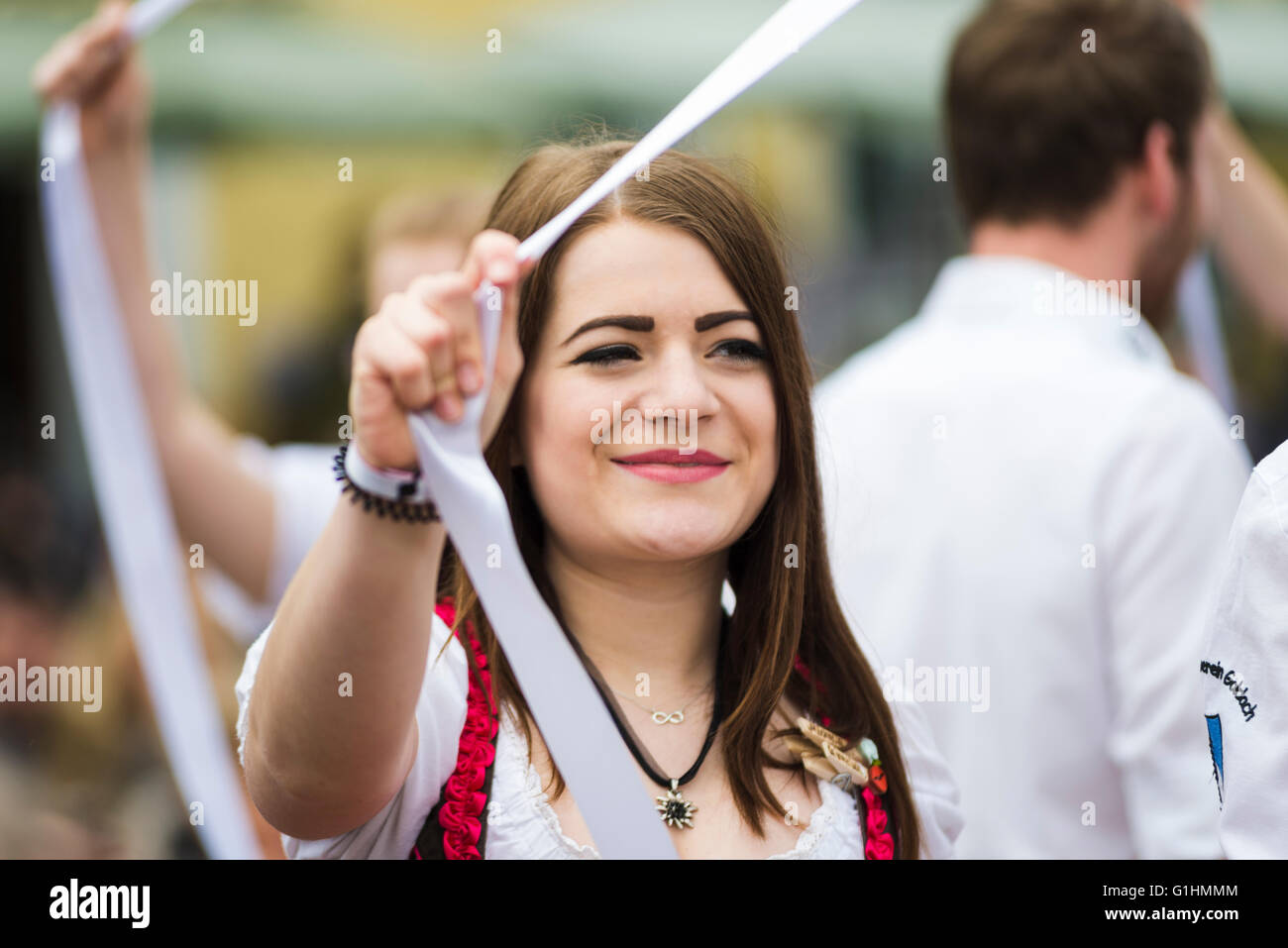 Porträt der lächelnde junge Frau in einem lokalen Kleid tanzen einen traditionellen Volkstanz um einen Maibaum hält ein weißes Band Stockfoto