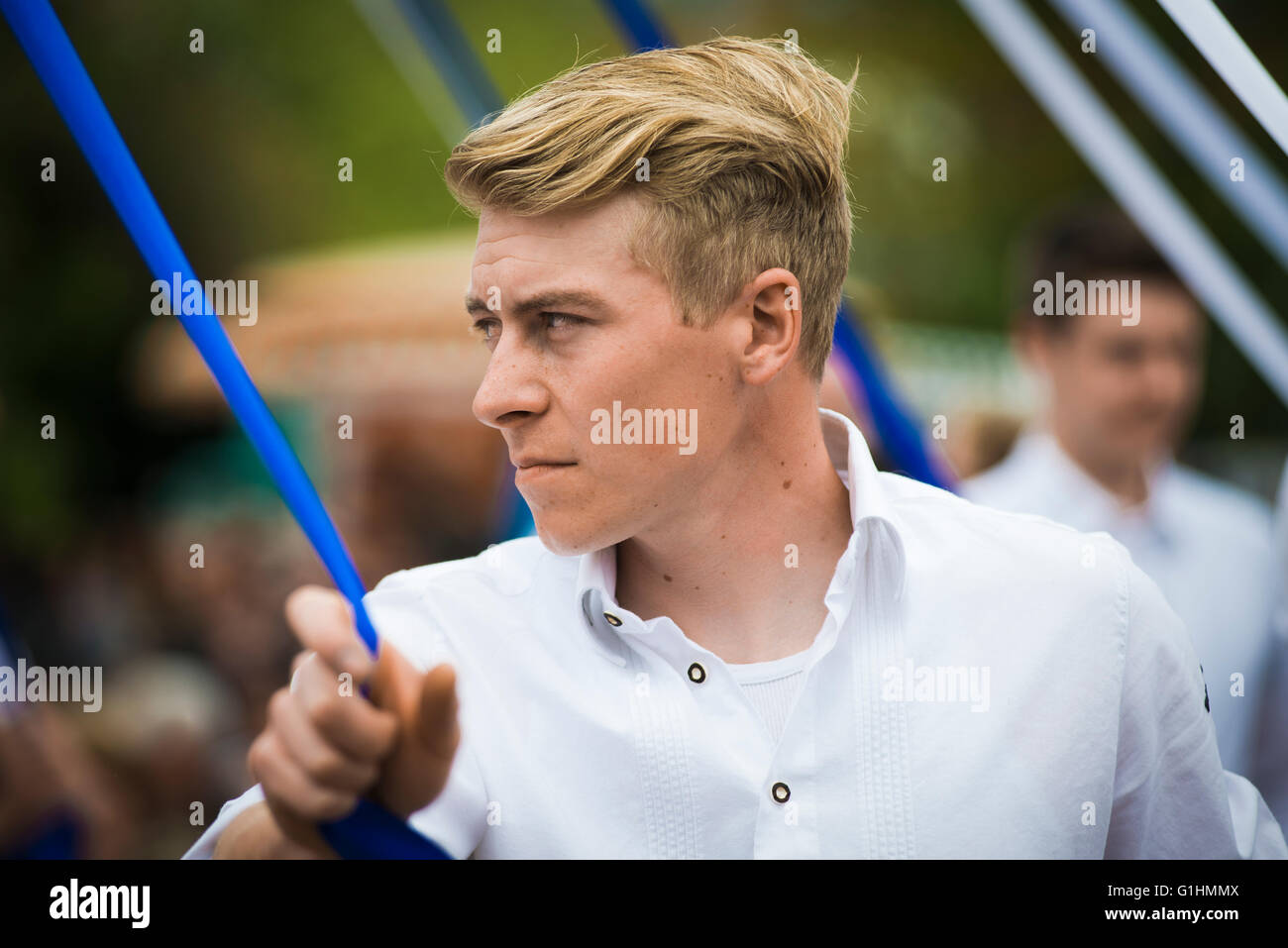 Porträt eines jungen Mannes im weißen Hemd tanzen einen traditionellen Volkstanz Bandltanz um einen Maibaum mit einem blauen Band Stockfoto