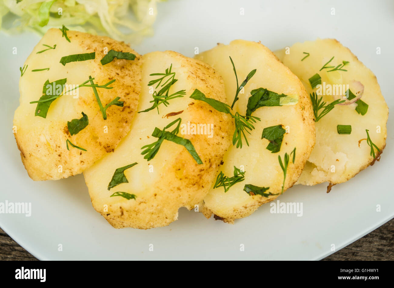 Köstliche geschnittene Kartoffelstücke perfekt zubereitet, aufgestapelt auf weißer Teller mit grünen Kräuter Aufstrich Stockfoto