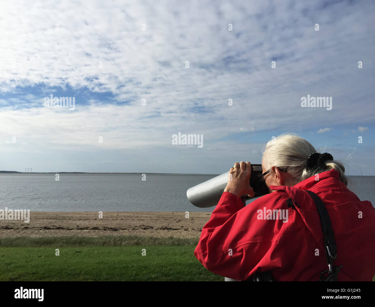 Senior-Frau am Strand mit Blick durch ein Fernglas, Esbjerg, Dänemark Stockfoto