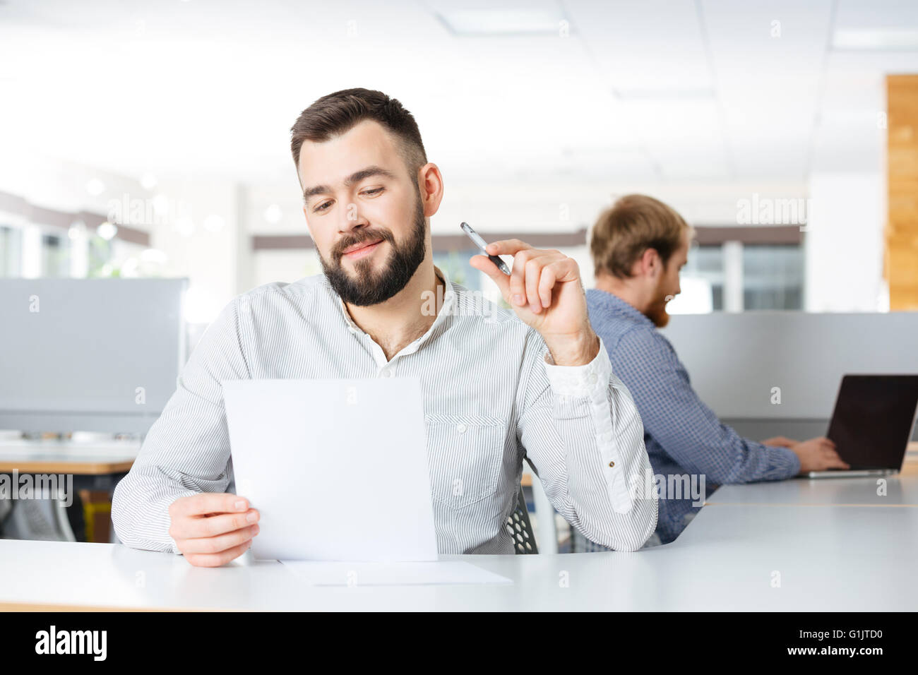 Glücklich bärtiger junger Geschäftsmann auf Arbeitsplatz sitzen und arbeiten mit Dokumenten Stockfoto