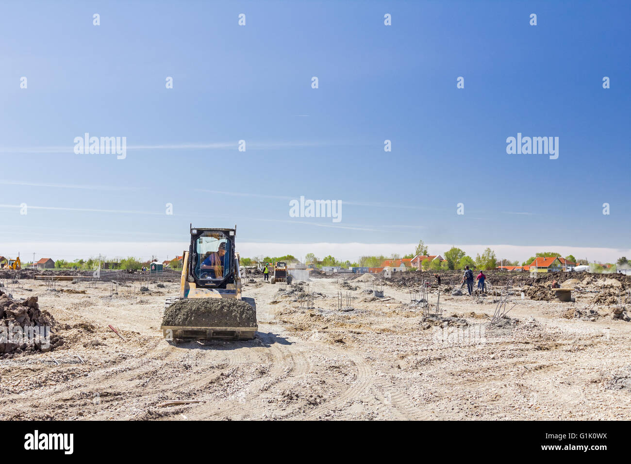 Kleine Bagger Bobcat ist Transport Kies in seinem Eimer über die Baustelle. Stockfoto