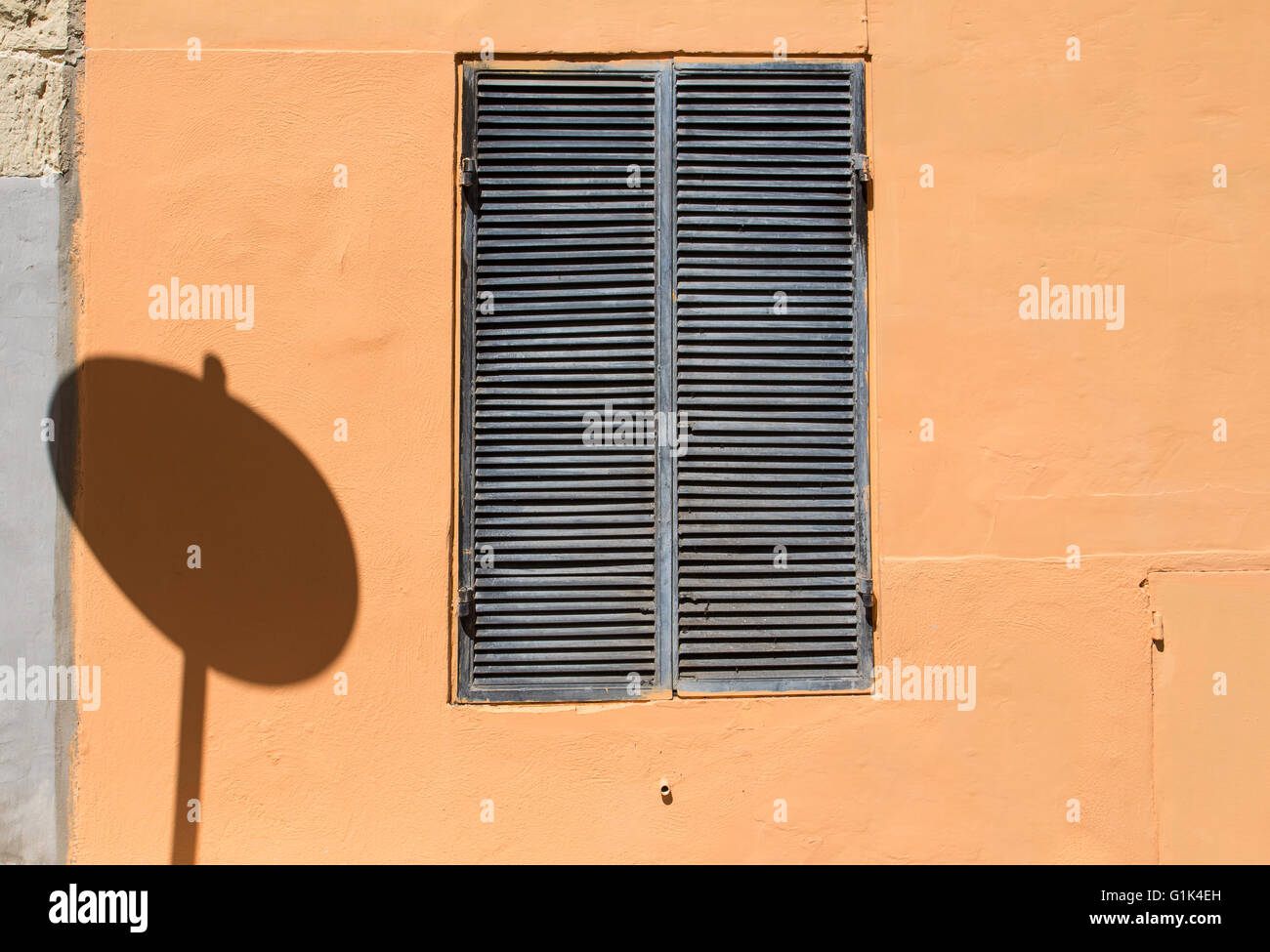 Hell orange Wand mit einem Fenster mit einem geschlossenen graues Gitter. Schatten der ein rundes Verkehrsschild des Fensters. Nur ein Schatten der Regel Stockfoto