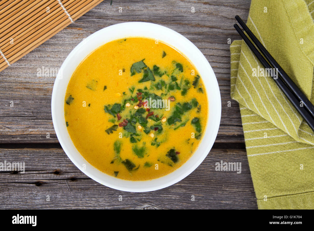 gelbes Thaicurry-Suppe mit Koriander auf rustikalen Tisch Stockfoto