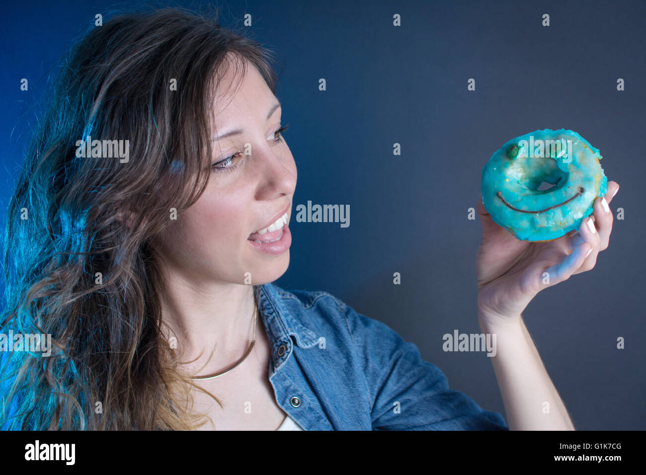 Mädchen hält einen blauen Smiley-Gesicht-Donut Stockfoto