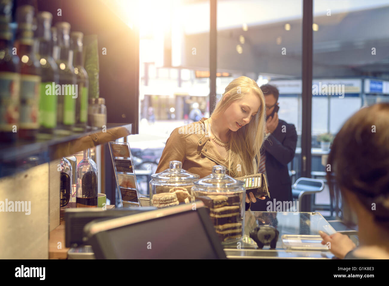 Blick über die Schulter der Kasse von einer attraktiven jungen blonden Frau die Zahlung an eine Kasse in ihrer Handtasche suchen Stockfoto