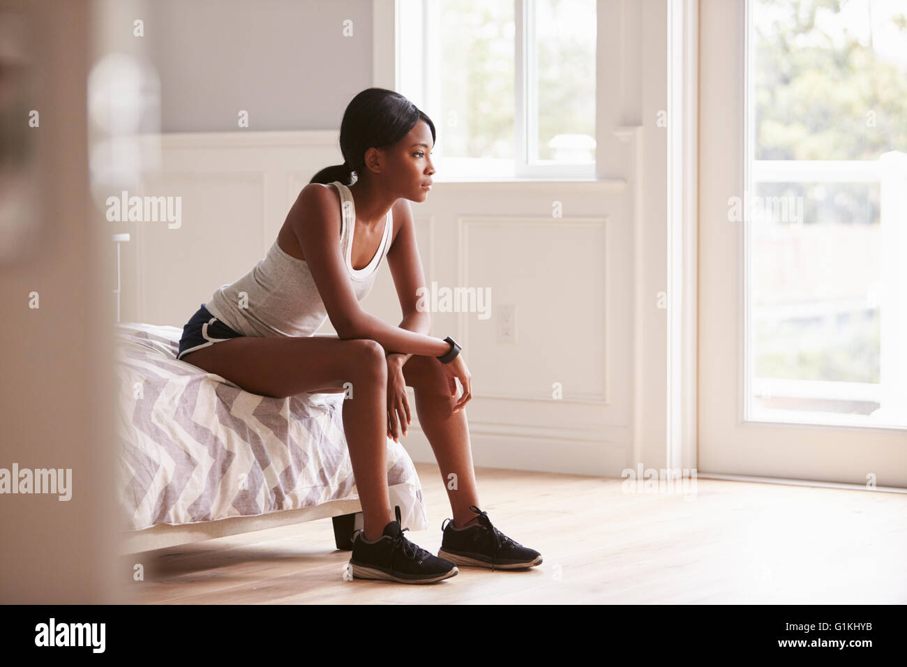 Junge schwarze Frau in Sportkleidung auf Bett zu Hause sitzen Stockfoto