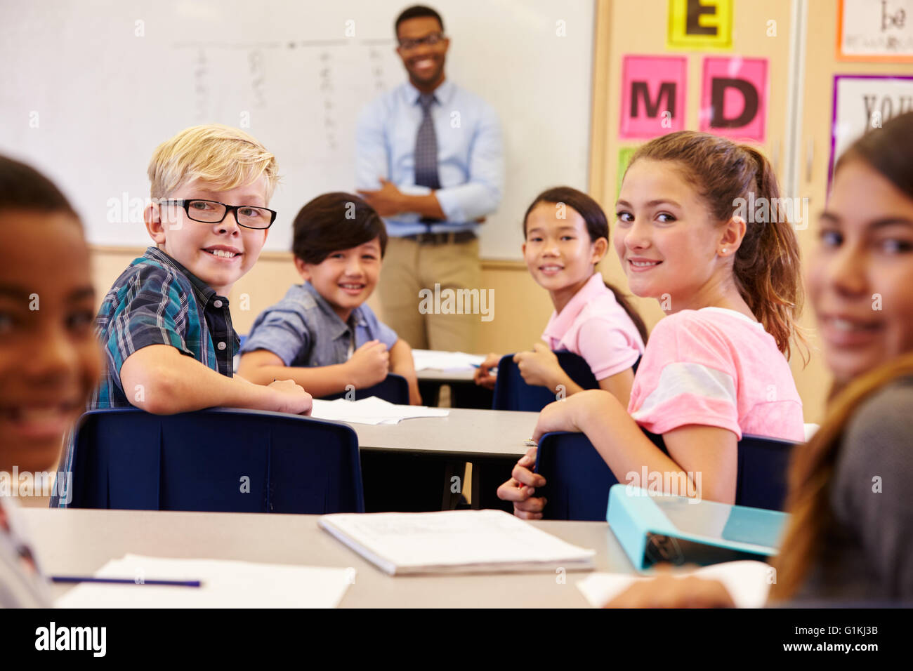 Kinder an ihren Schreibtischen im Klassenzimmer drehen vor der Kamera Stockfoto