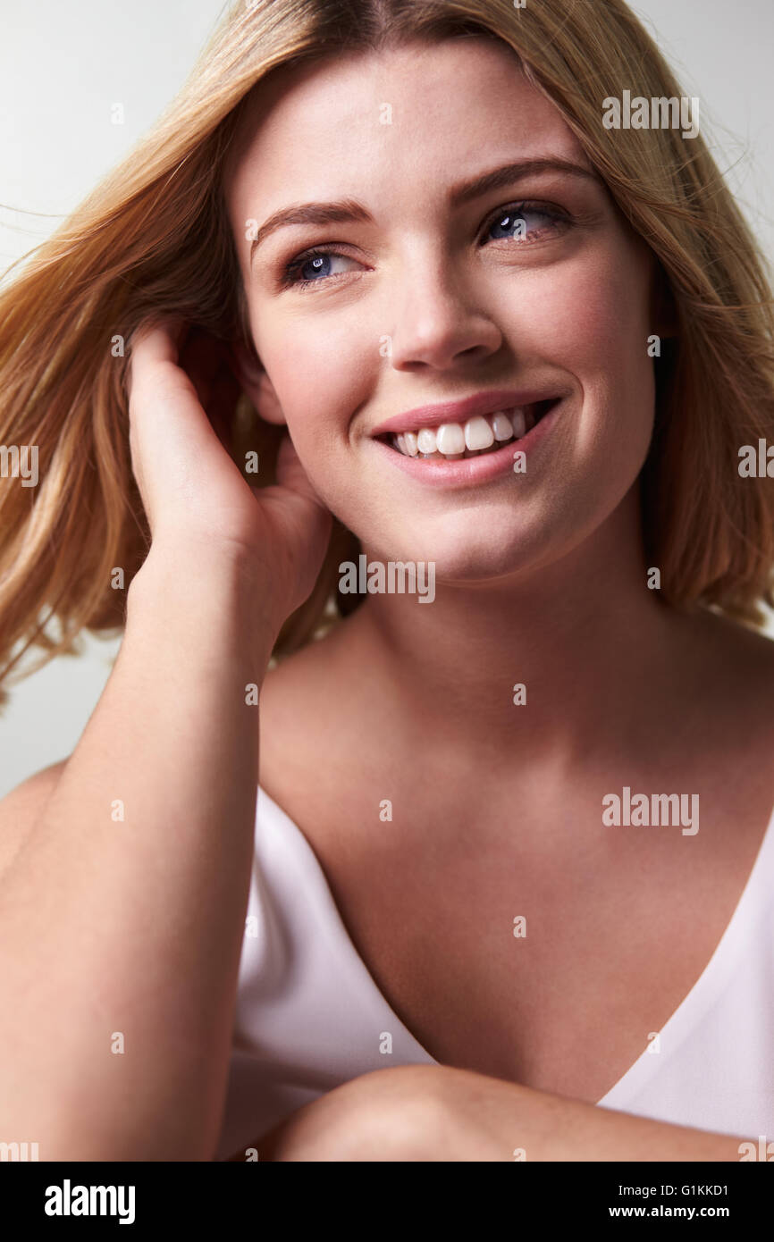Lächelnde blonde Frau wegsehen, berühren Haar, vertikale Stockfoto