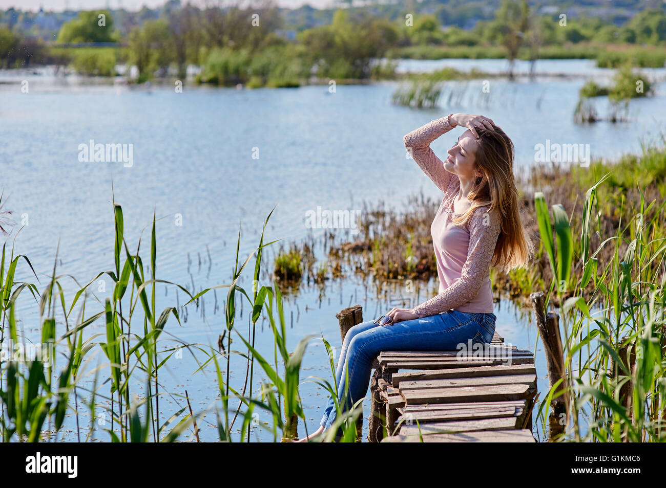 schöne Frau sitzen auf hölzerne Pier am Fluss Stockfoto