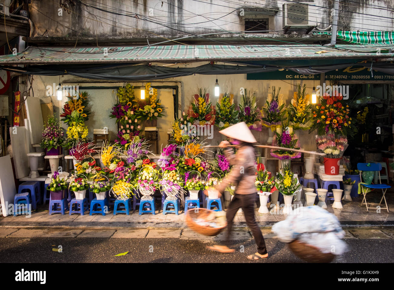 Eine Straße Verkäufer geht vorbei an einem Floristen Display Cau unterwegs in der Altstadt von Hanoi, Vietnam Stockfoto