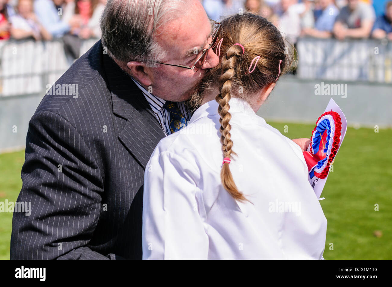 Ein junges Mädchen wendet sich ihr Kopf ab wie ein Richter ihr einen unschuldigen Kuss auf die Wange gibt nach dem Gewinn eines Wettbewerbs. Stockfoto