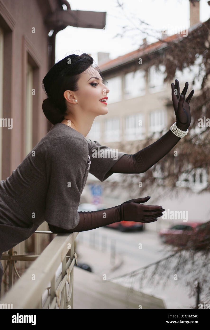 Schöne Frau im Retro-Kleid winken vom Balkon Stockfoto