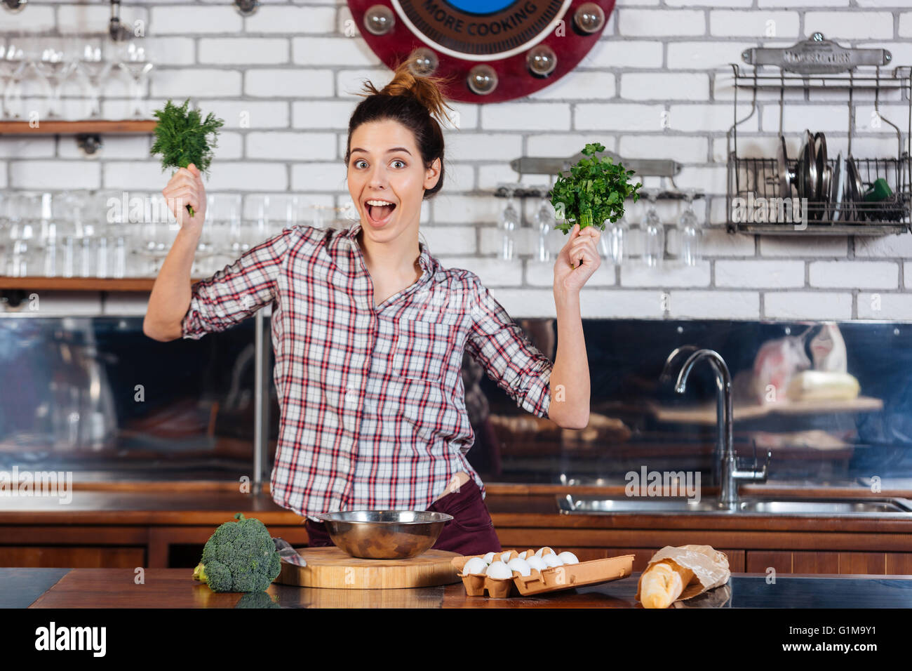 Cheerul hübsche junge Frau mit Dill und Petersilie in der Küche Stockfoto