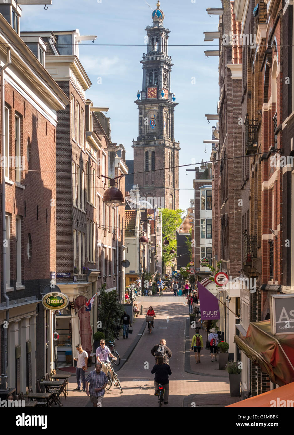 Amsterdam Jordaan. Straße und Brücke im Stadtteil Jordaan mit Radfahrern, Radfahren in der Sonne. Westertoren im Hintergrund. Stockfoto