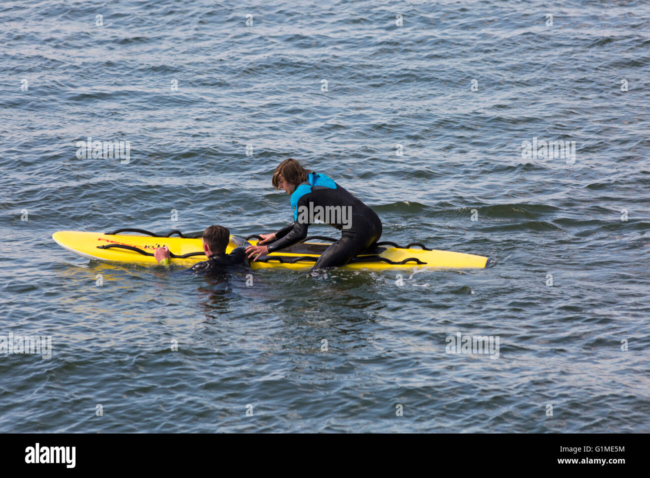 RNLI-Rettungsschwimmer, der im Mai im Rahmen einer Trainingsübung in Bournemouth, Dorset, Großbritannien, einen Mann vom Wasser auf das Surfbrett mit dem „Rettungsschlitten“ am Strand von Bournemouth zieht Stockfoto