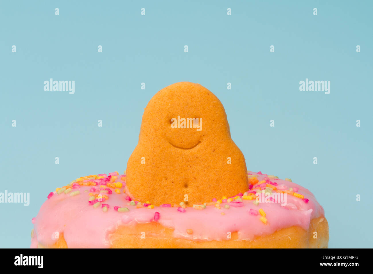 Eine glückliche, lachende Lebkuchenmann sitzen in das Loch ein Kuchen mit rosa Zuckerguss und Streusel auf eine isolierte blauem Hintergrund Stockfoto