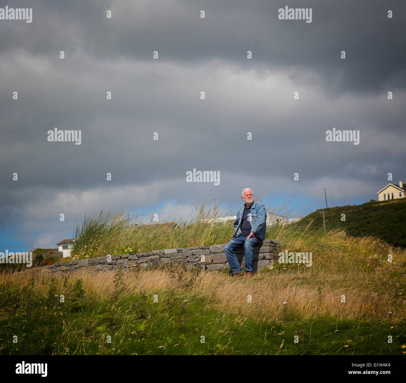 Ältere Mann sitzt entlang auf Steinmauer am Inchydoney Beach in der Nähe von Clonakilty, County Cork, Irland.  Eire. Stockfoto