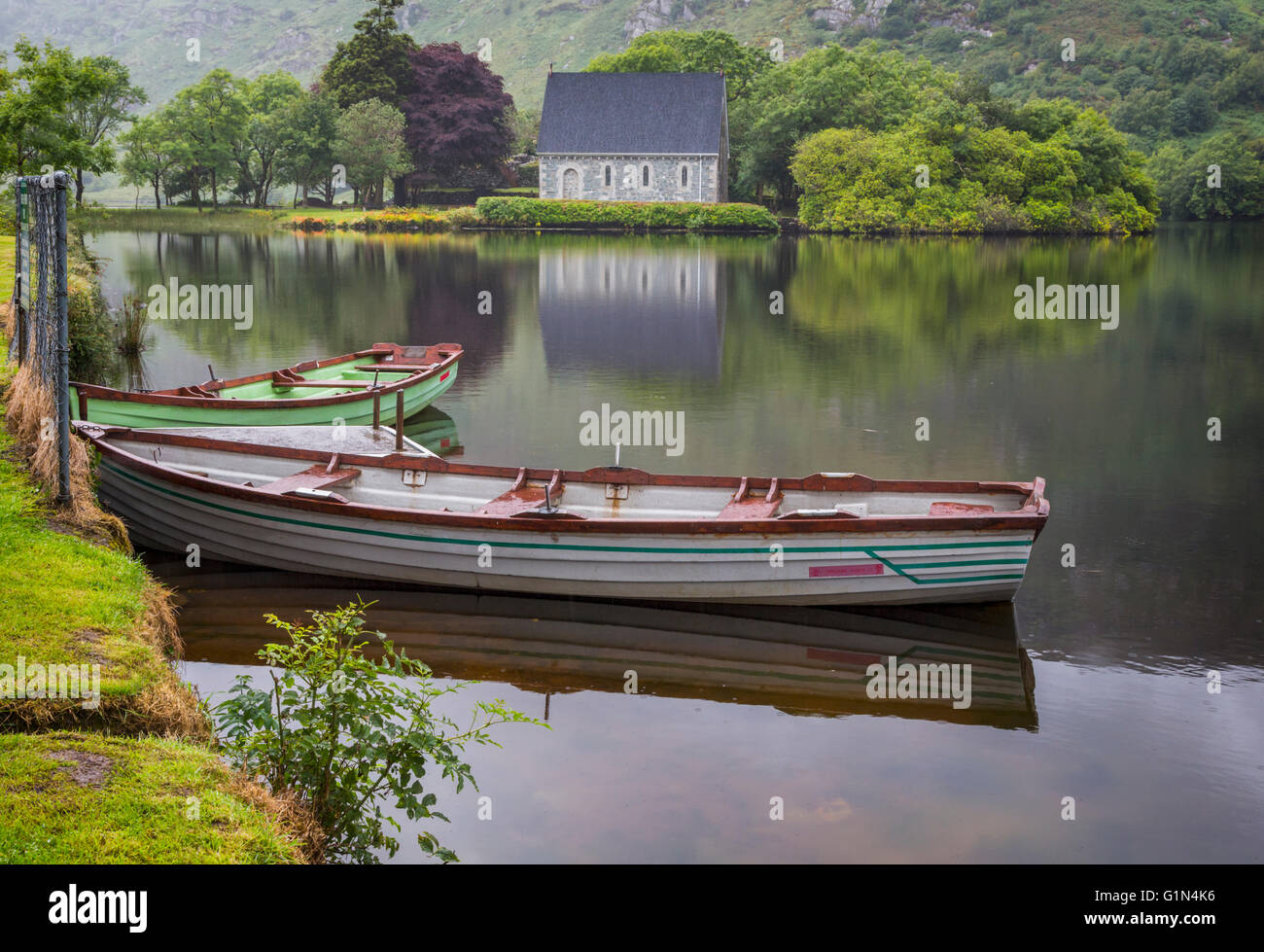 Gougane Barra, County Cork, Irland.  Eire.  Blick über Ruderboote vertäut am Ufer Sees mit der Eremitage Stockfoto