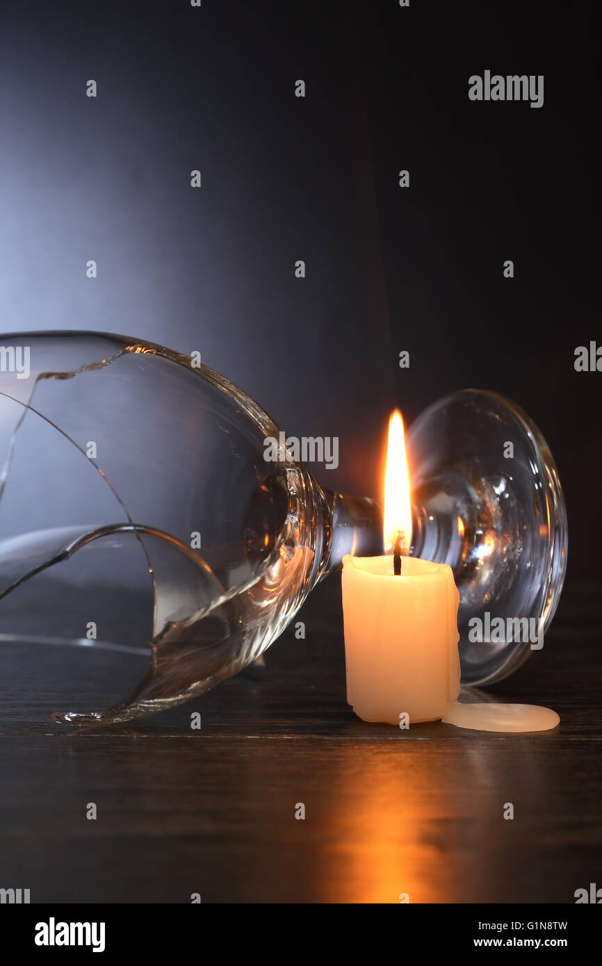 Weinglas in der Nähe von Beleuchtung Kerze auf dunklem Hintergrund gebrochen Stockfoto