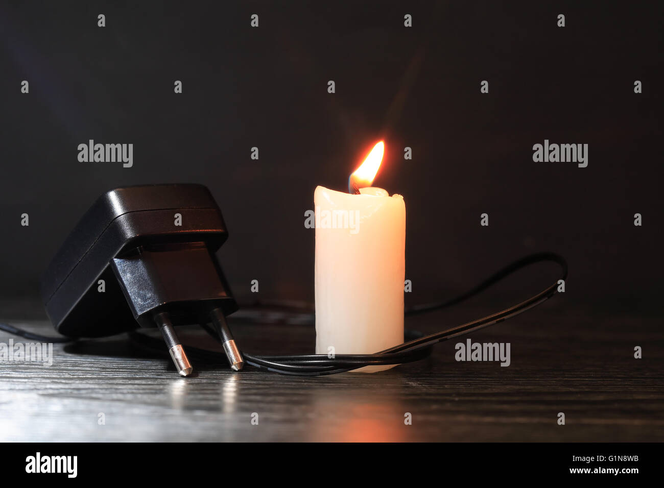 Blackout-Konzept. Elektro-Ladegerät mit Kabel in der Nähe von Beleuchtung Kerze auf dunklem Hintergrund Stockfoto