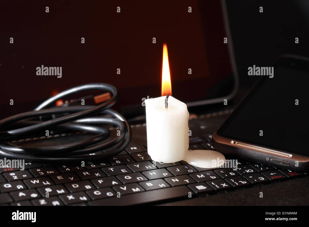 Blackout-Konzept. Kerze anzünden auf Laptop in der Nähe von Kabel Stockfoto