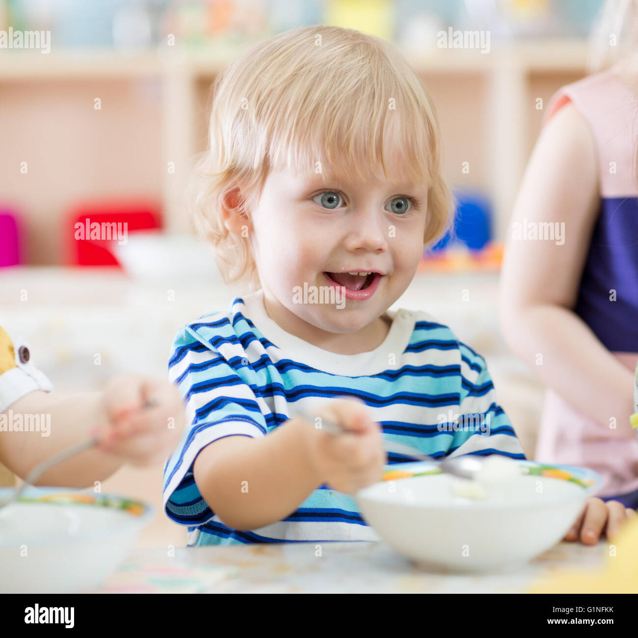 lustig lächelndes Kind Essen vom Teller im kindergarten Stockfoto