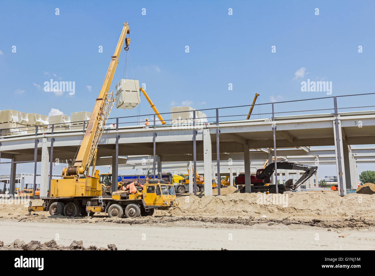 Mobilkran wird Ladung geladen. Blick auf Baustelle mit Maschinen, Menschen bei der Arbeit. Stockfoto