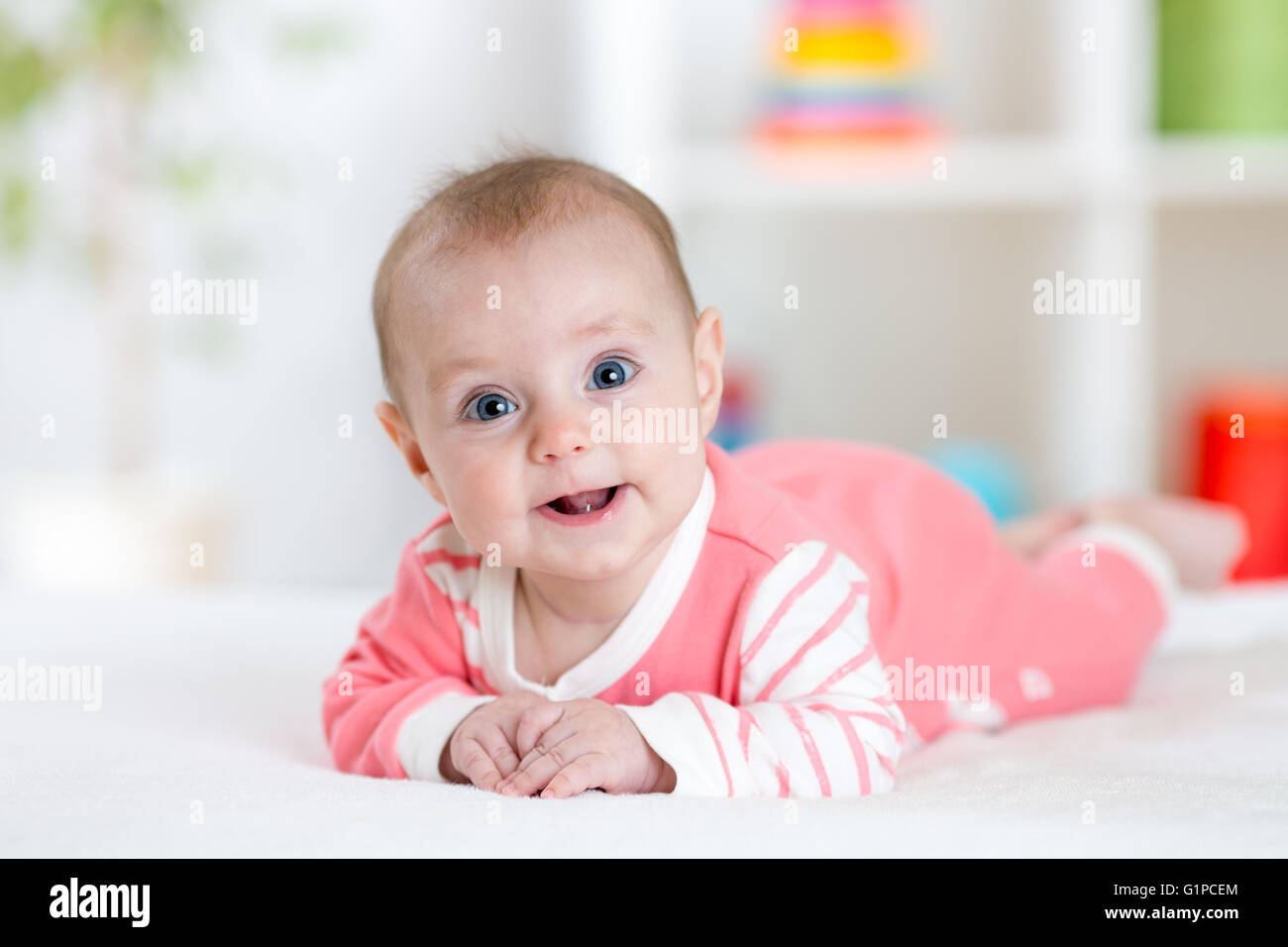 Sehr glücklich lachendes Baby in Rosa Kleidung auf dem Bauch liegend. Säugling direkt in die Kamera schaut Stockfoto