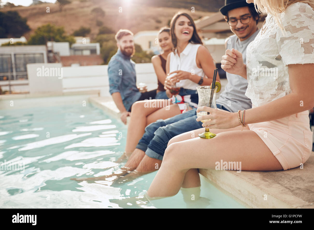 Schuss von Jugendlichen tranken Cocktails am Pool. Freunde am Rande des Pools mit Füßen im Wasser sitzen. Entspannen Stockfoto