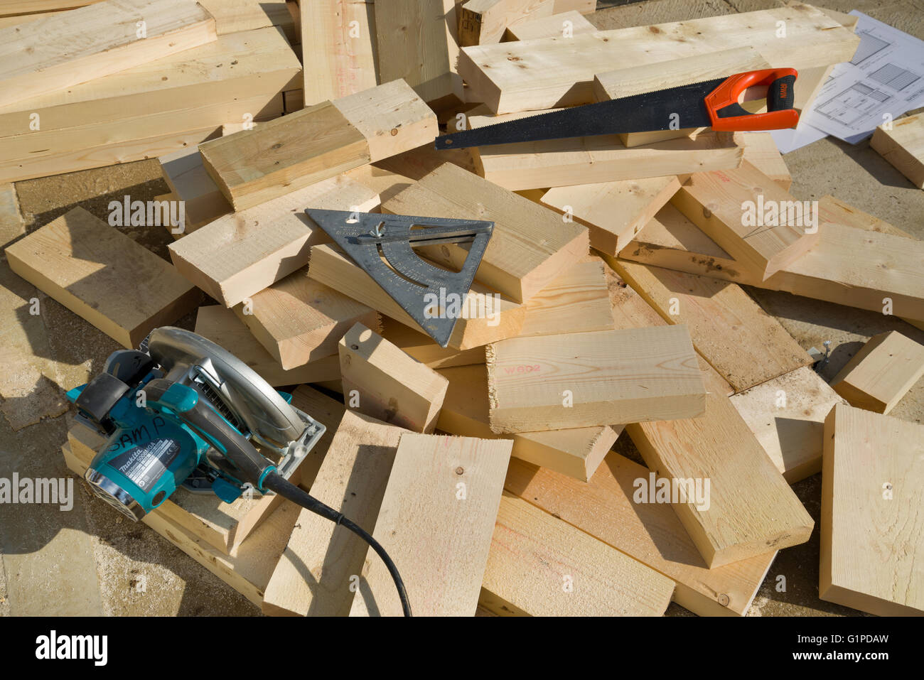 Nadelschnittholz schneidet mit Kreissäge, Säge und Sparren Quadrat. Architekten-Pläne im Hintergrund. Stockfoto